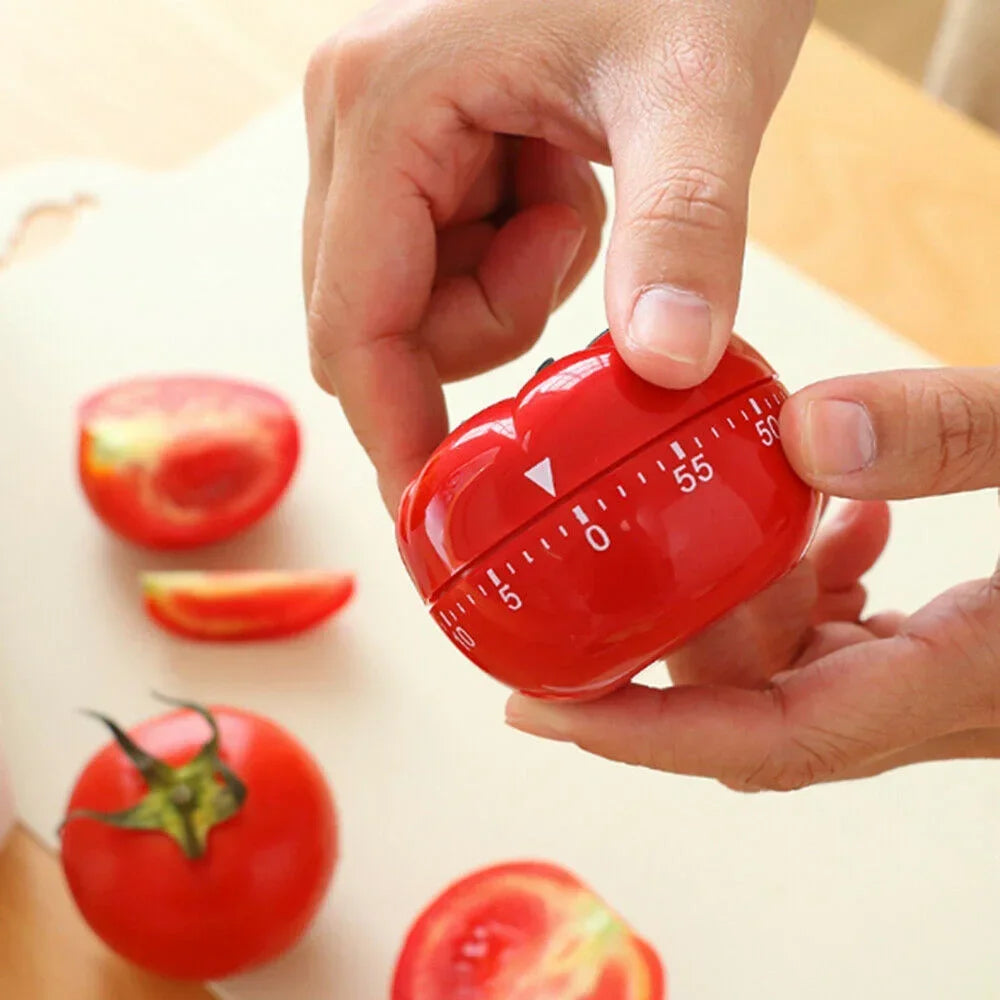 Red kitchen timer held by a hand with tomatoes in the background